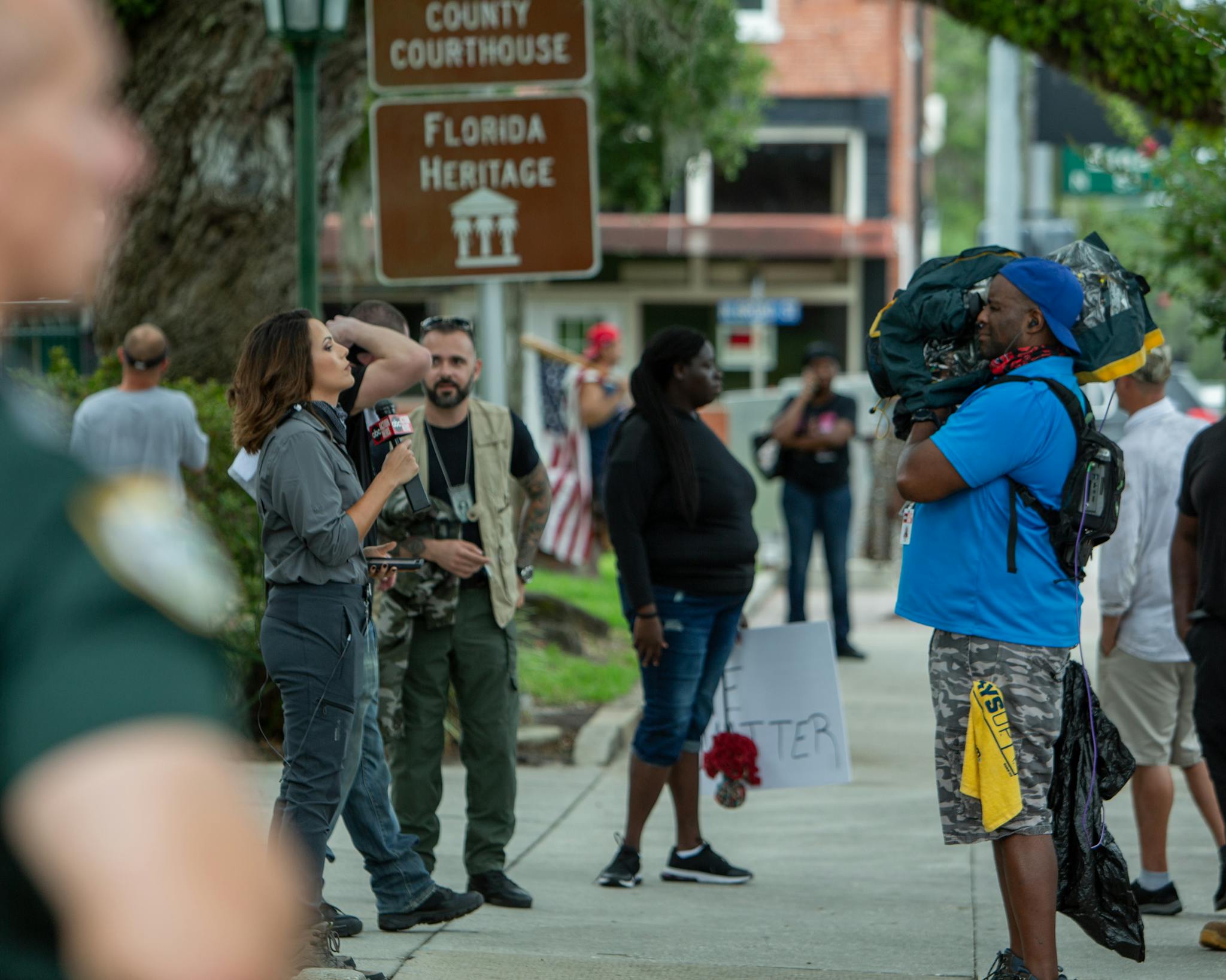 A street protest in Brooksville, FL with journalists and demonstrators captured outdoors.