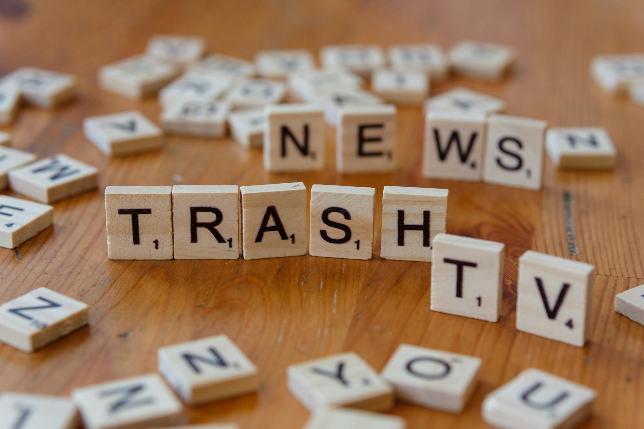 Close-up of wooden letter tiles spelling out Trash TV News on a table.